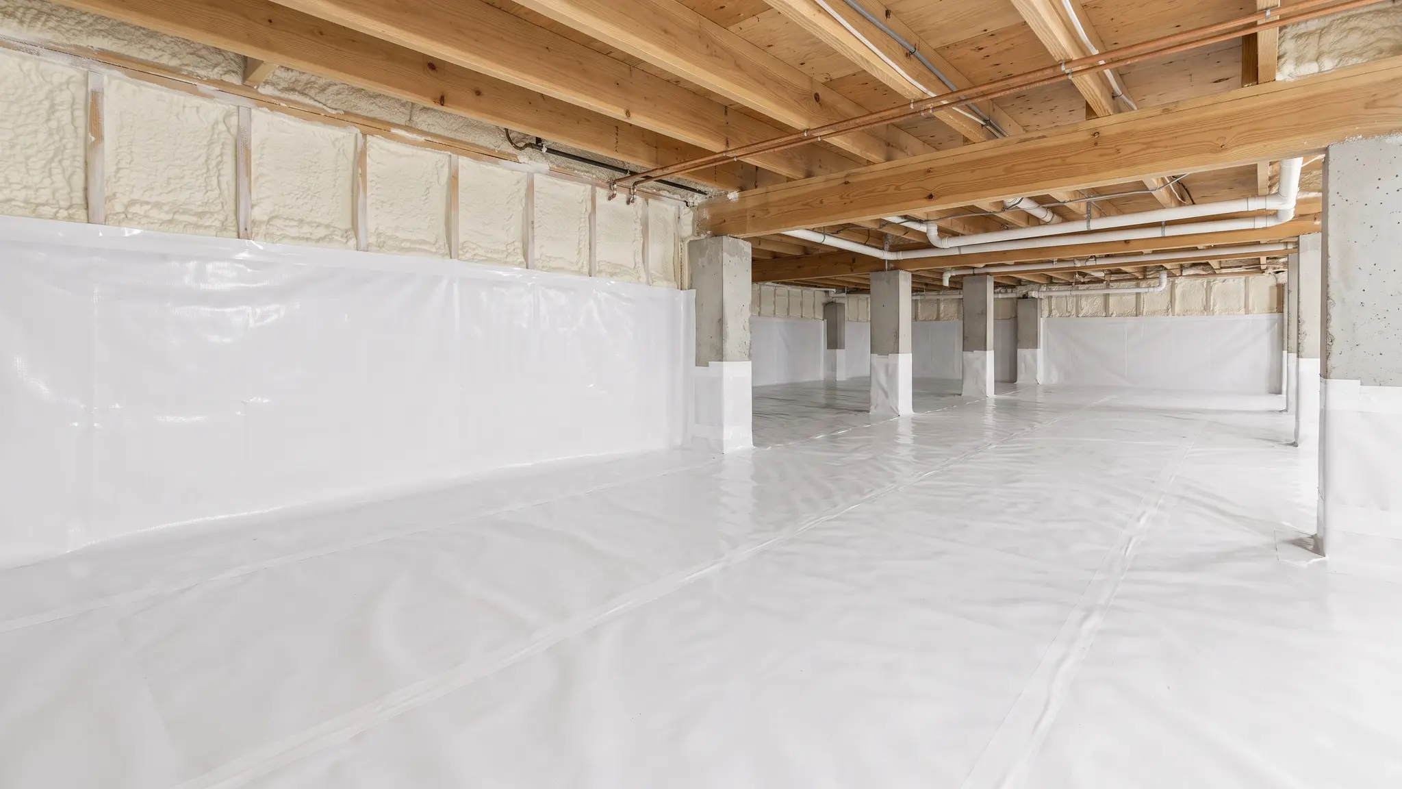A clean encapsulated crawl space with a white vapor barrier on the floor and walls, an insulated rim joist and bright lighting