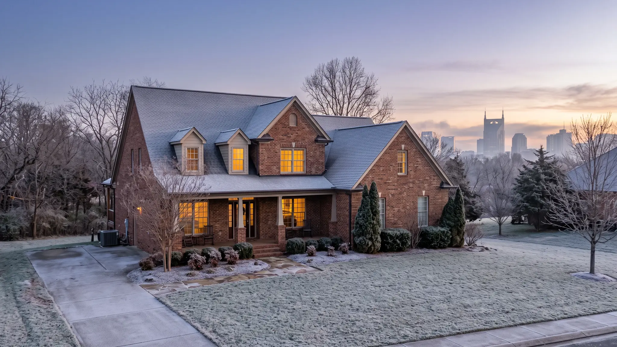 Music City Insulation | Insulation in Nashville, TN A cozy brick Tennessee home with warm lit windows on a frosty winter dawn, light frost on the roof and lawn, with the Nashville skyline softly visible in the distance